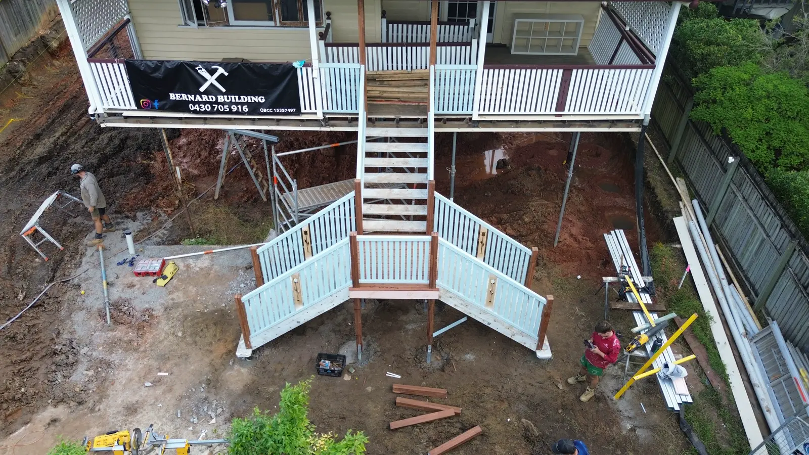 New external timber stairs mid-build under a high-set Brisbane home, Bernard Building banner on the verandah